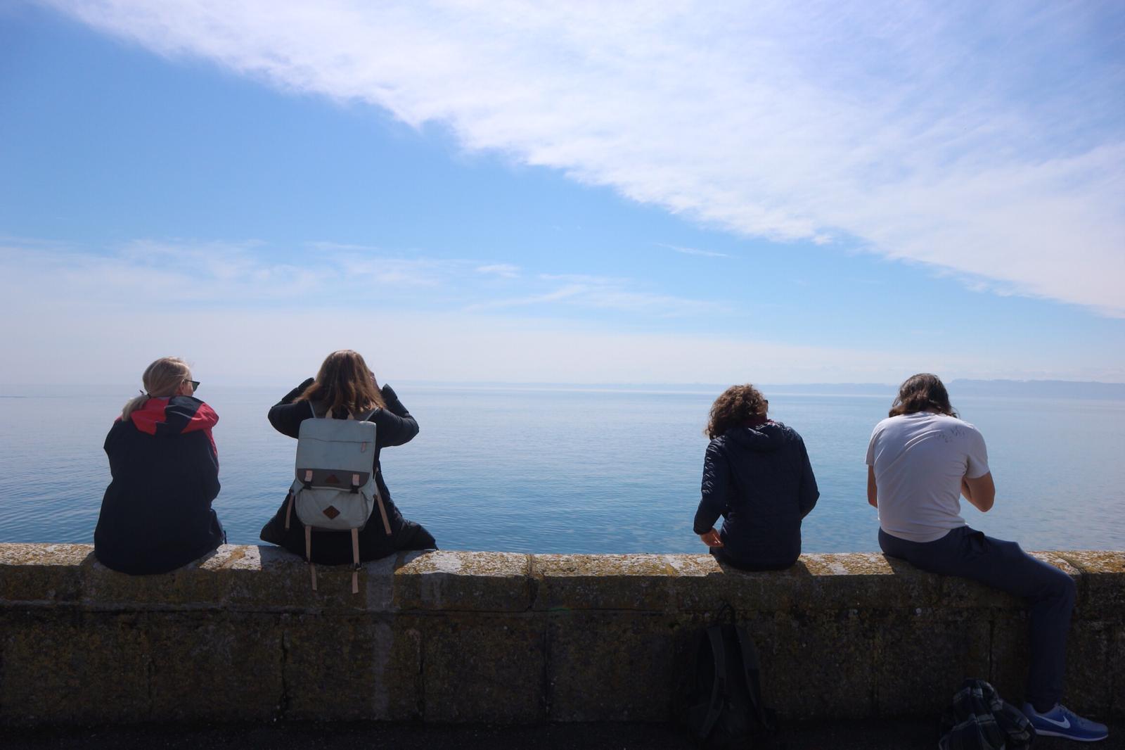 students sitting on a ledge looking at the ocean